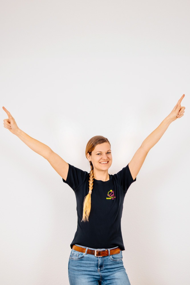 Barf Hunde-Ernährungsberaterin Teresa von BARF Concept trägt schwarzes Shirt, zeigt mit beiden Händen und Zeigefinger nach oben, geflochtene Haare