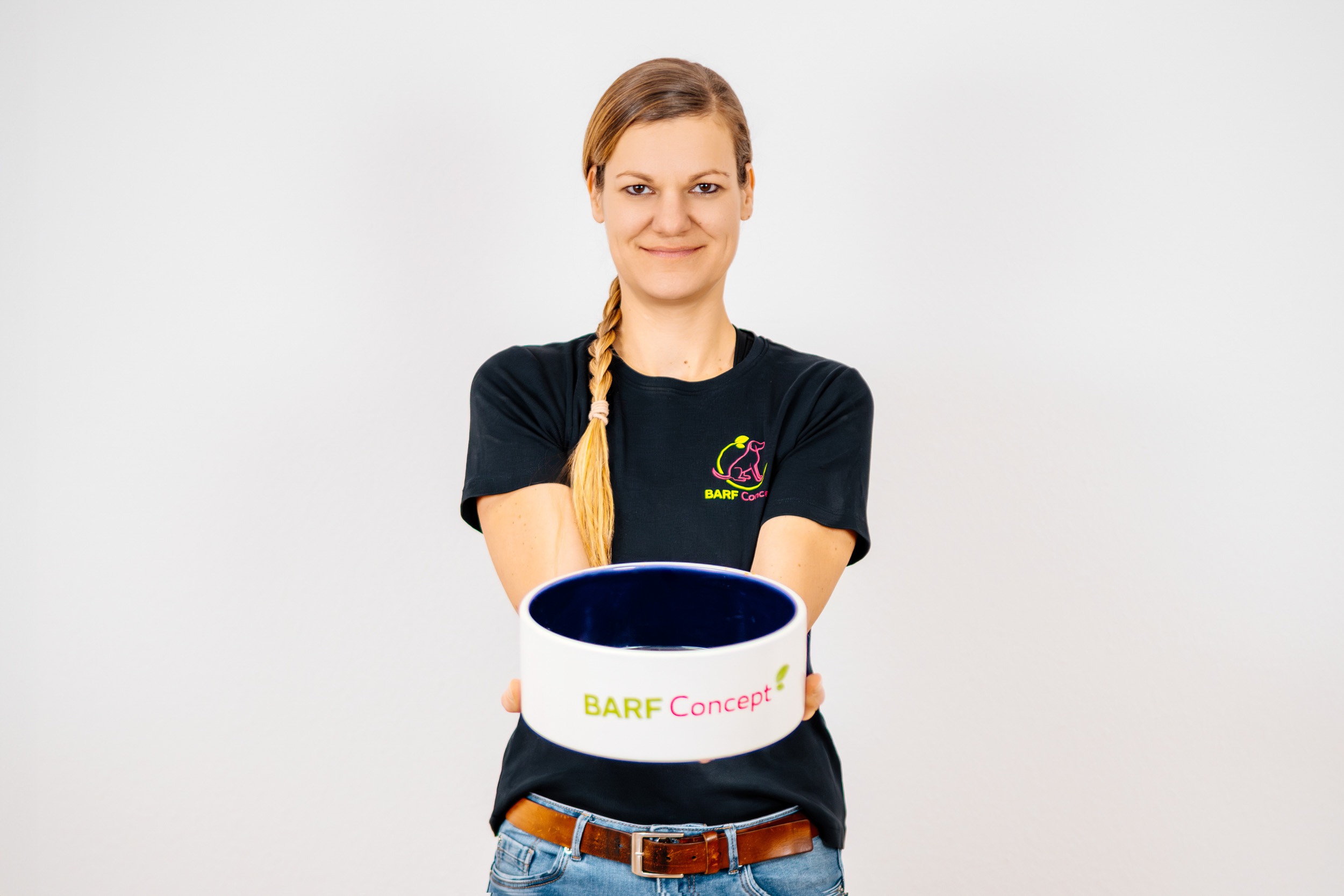 BARF-Concept Hundeernährungsberatung Teresa trägt schwarzes Tshirt, geflochtene Haare, hält Hundenapf nach vorne